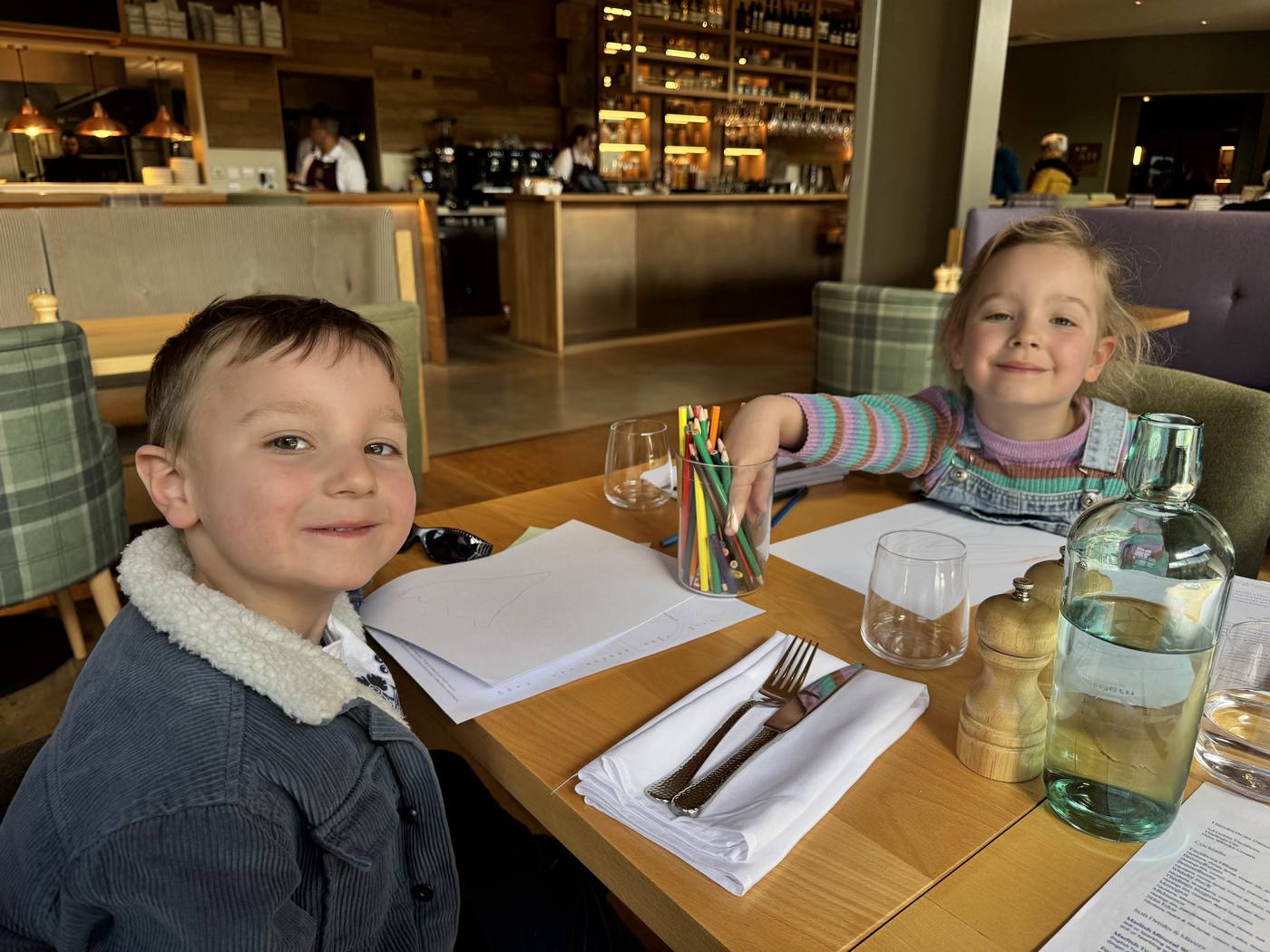 Two smiling children at a restaurant table with paper and a pot of colouring pencils at Ad Gefrin in Wooler.