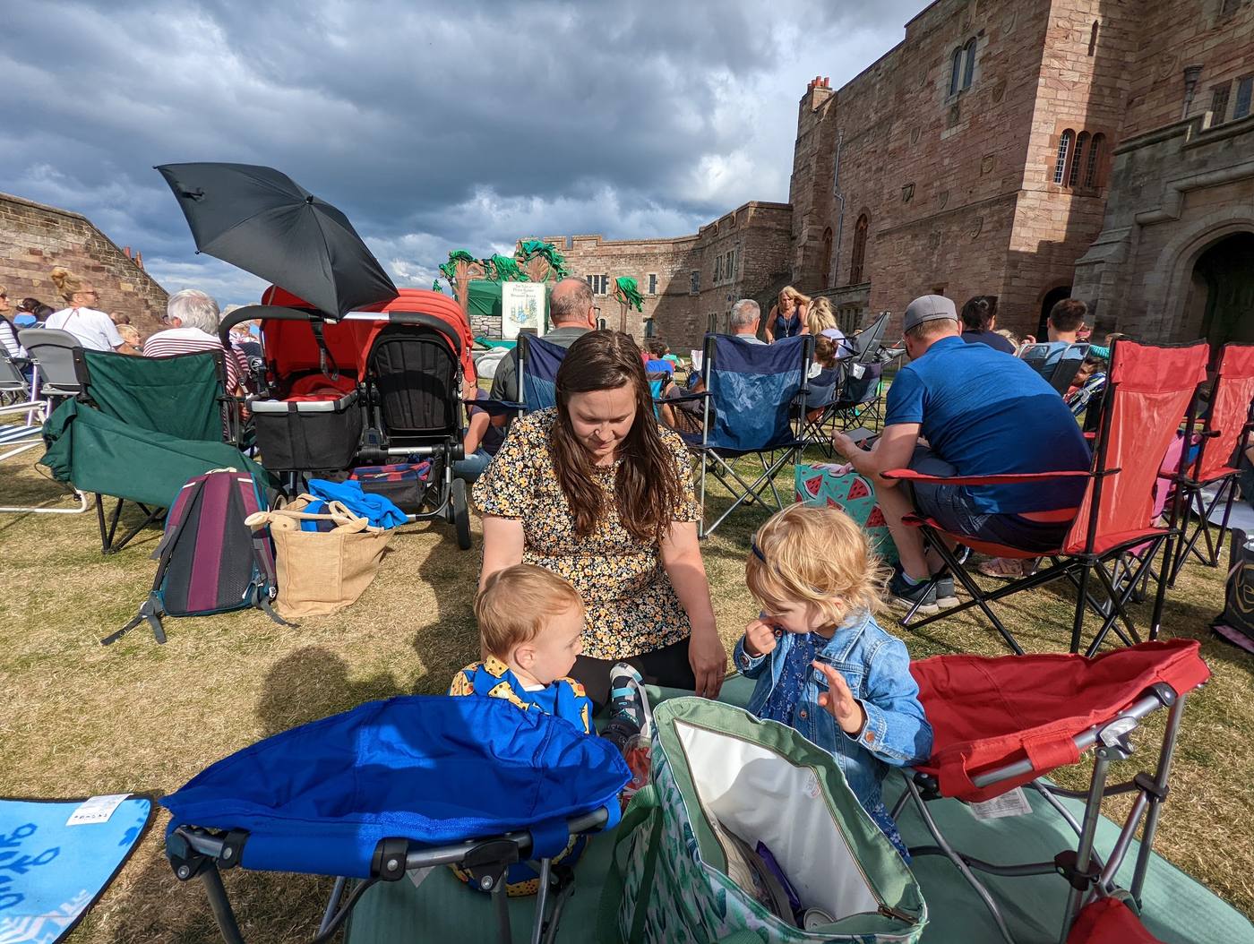 A family on a picnic blanket among camping chairs in the courtyard at Bamburgh Castle, waiting for an outdoor play to start.