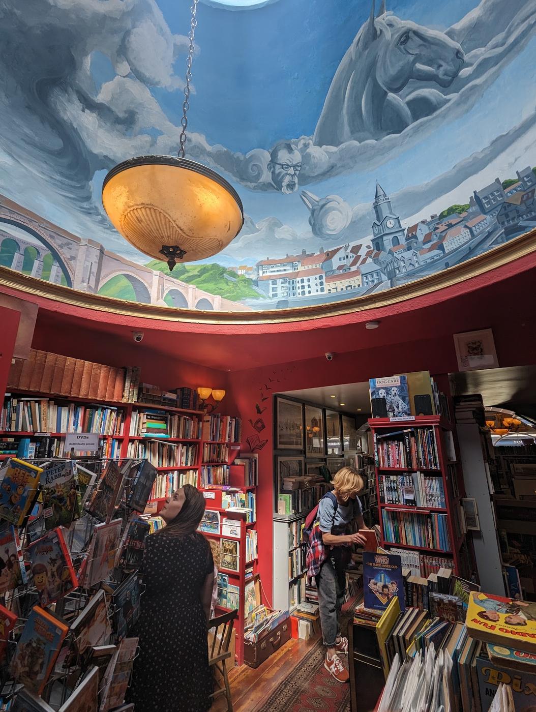 Inside Slightly Foxed bookshop in Berwick, with red shelves and a domed ceiling painted with the Royal Border Bridge and the Town Hall.