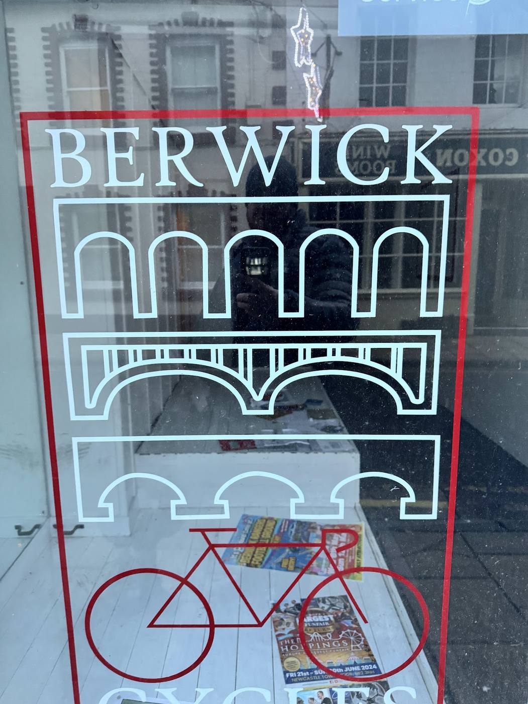 The window of Berwick Cycles, with a sign showing Berwick's three bridges above a red bicycle.