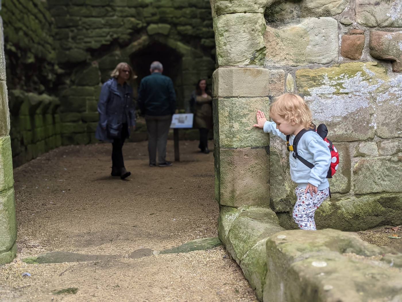 A toddler with a small backpack touching the old stone walls inside the ruins of Etal Castle.