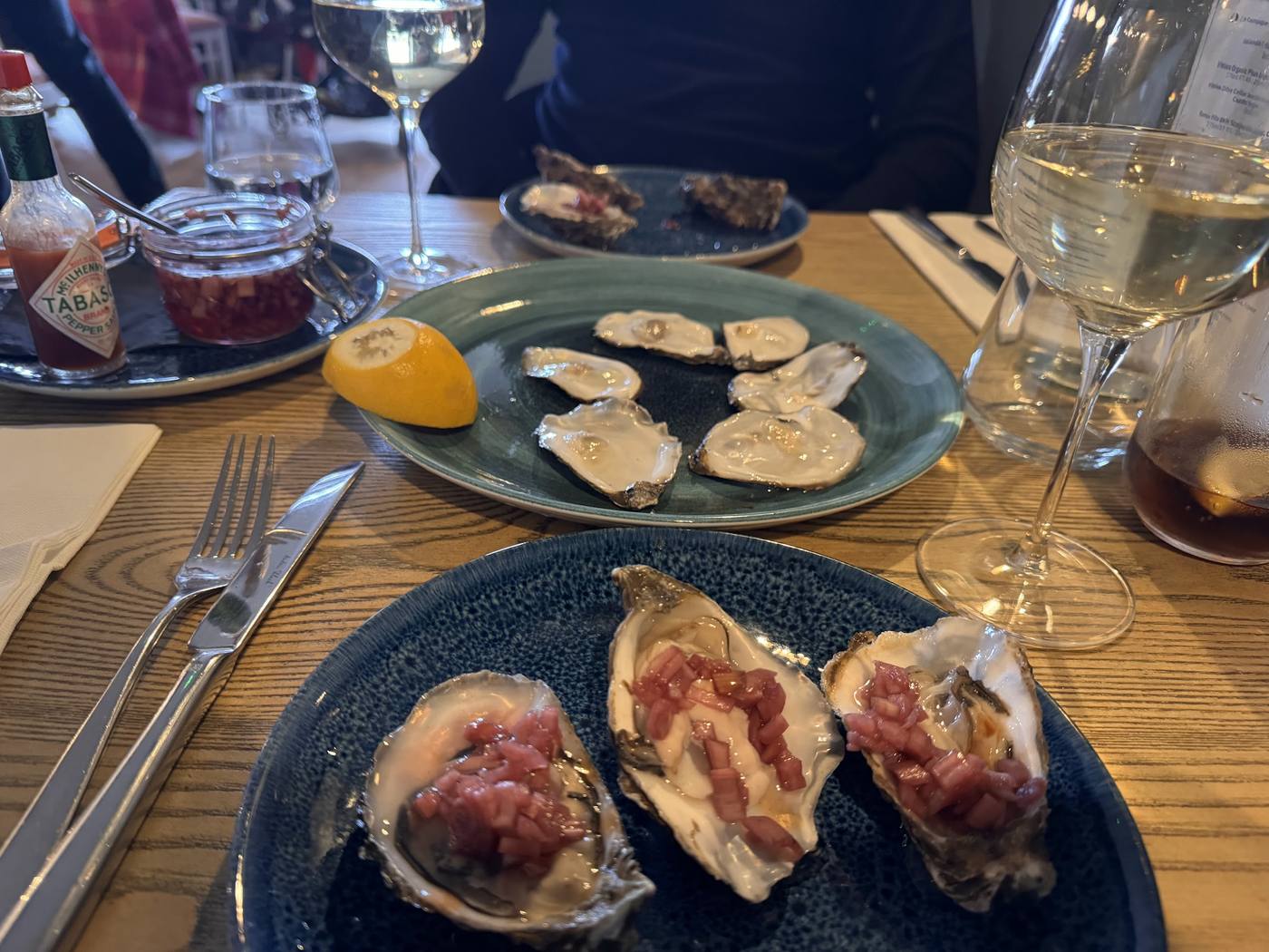 Plates of oysters with shallot vinegar and a glass of white wine on a table at The Potted Lobster, Bamburgh.