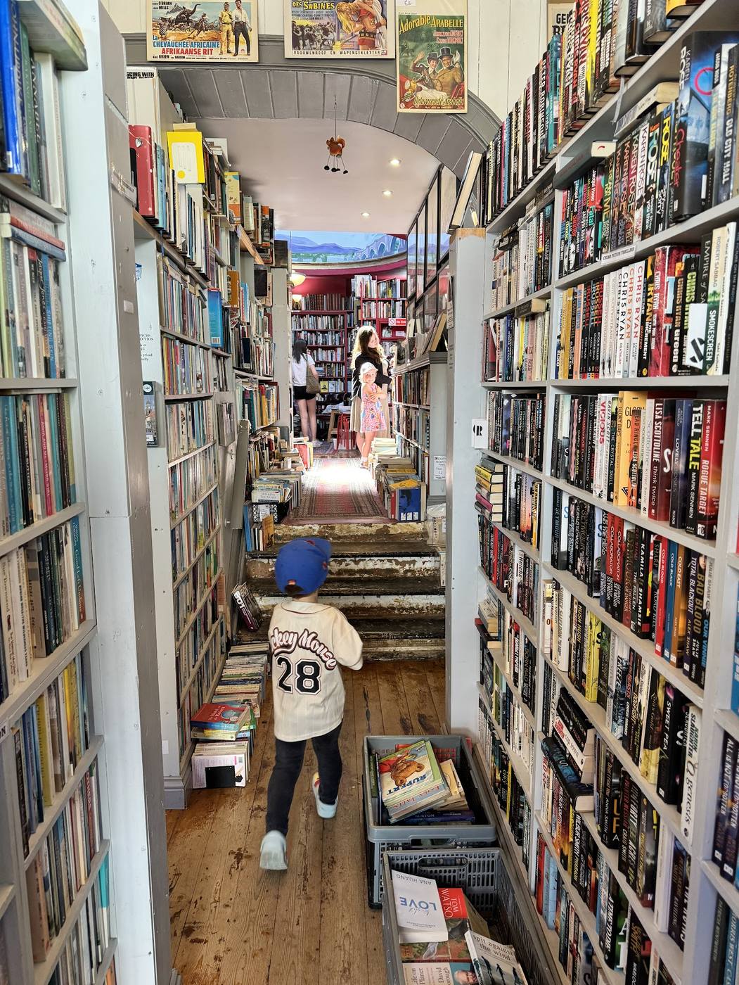 A small boy walking down a long, narrow aisle of packed bookshelves at Slightly Foxed in Berwick.