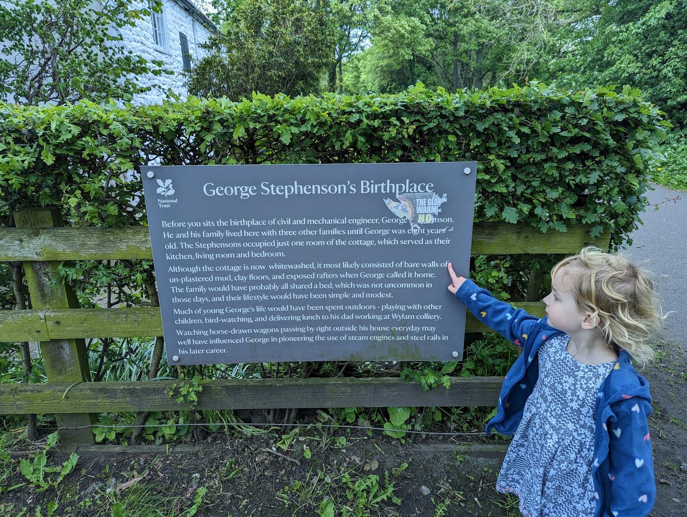 A child pointing at the National Trust sign for George Stephenson's Birthplace.