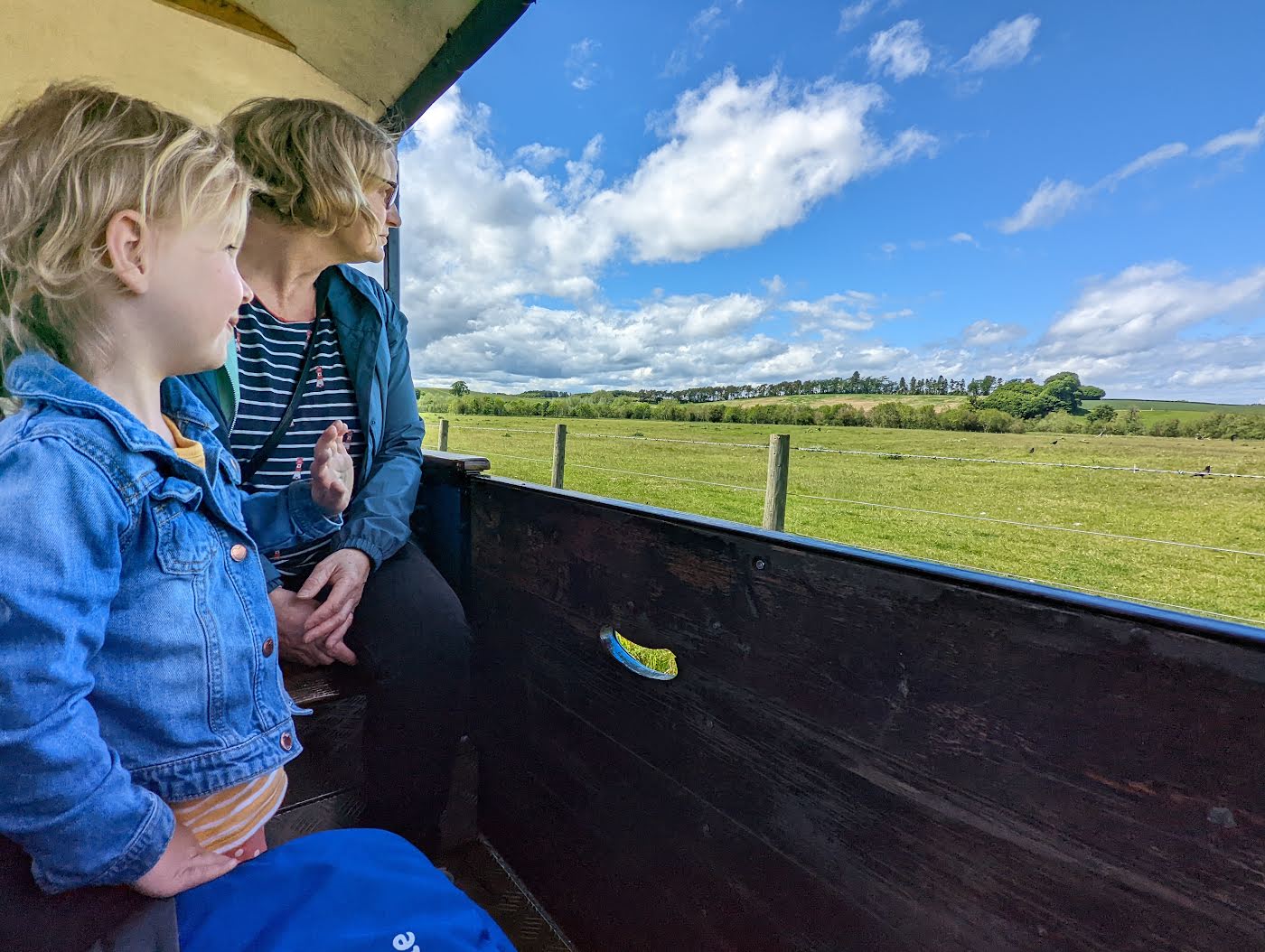 Two young children sitting in an open carriage of the Heatherslaw Light Railway, with fields and a big blue sky outside.
